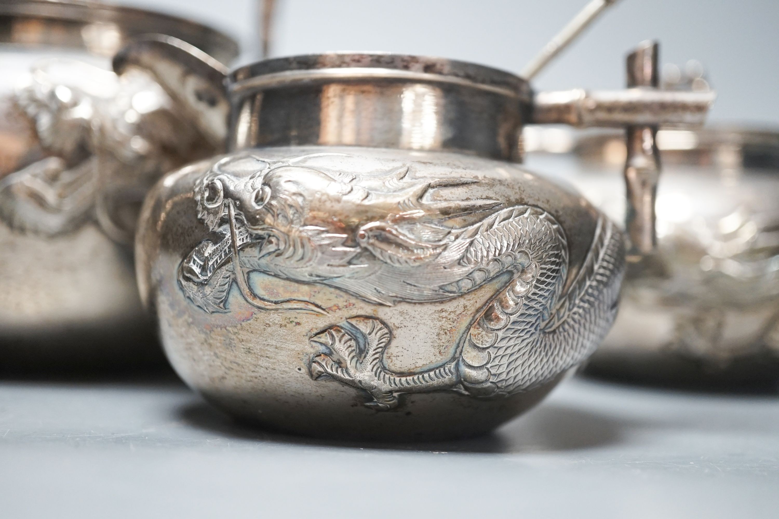 A Chinese white metal three piece tea set, with embossed dragon decoration and faux bamboo handles, teapot height, 17.8cm, gross 28.5oz (a.f.) and a similar spoon.